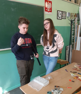 widzimy chłopca tłumaczącego dziewczynie jak obsługiwać wędkę 