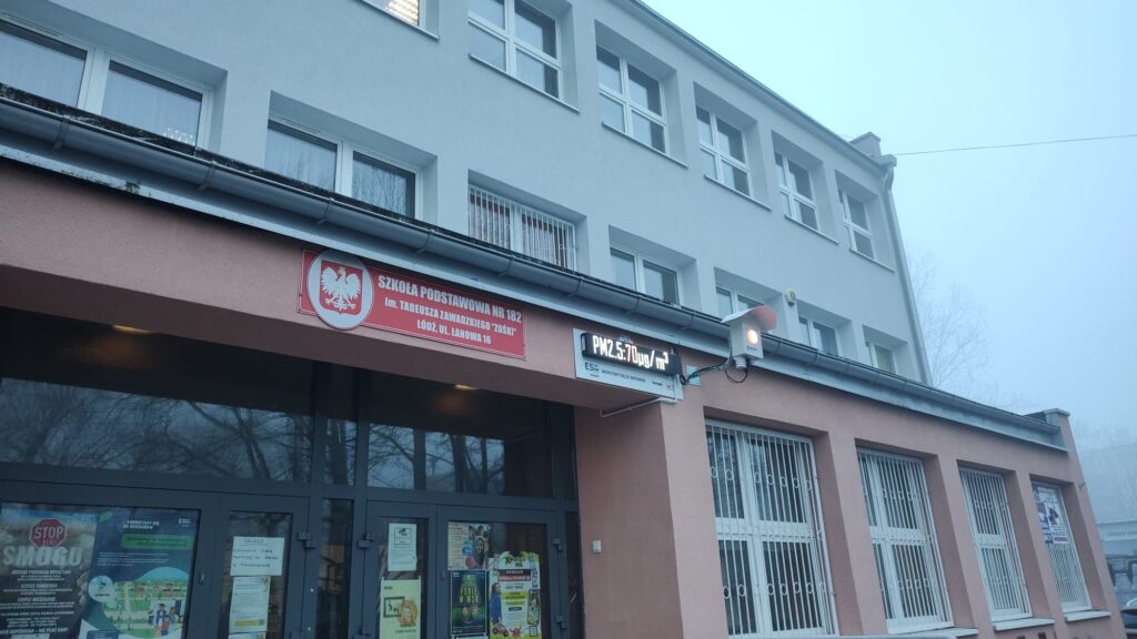Na zdjęciu widać czujnik informujący o jakości powietrza i stężenia pyłów PM2,5 oraz PM10 zamontowany przy wejściu do szkoły.