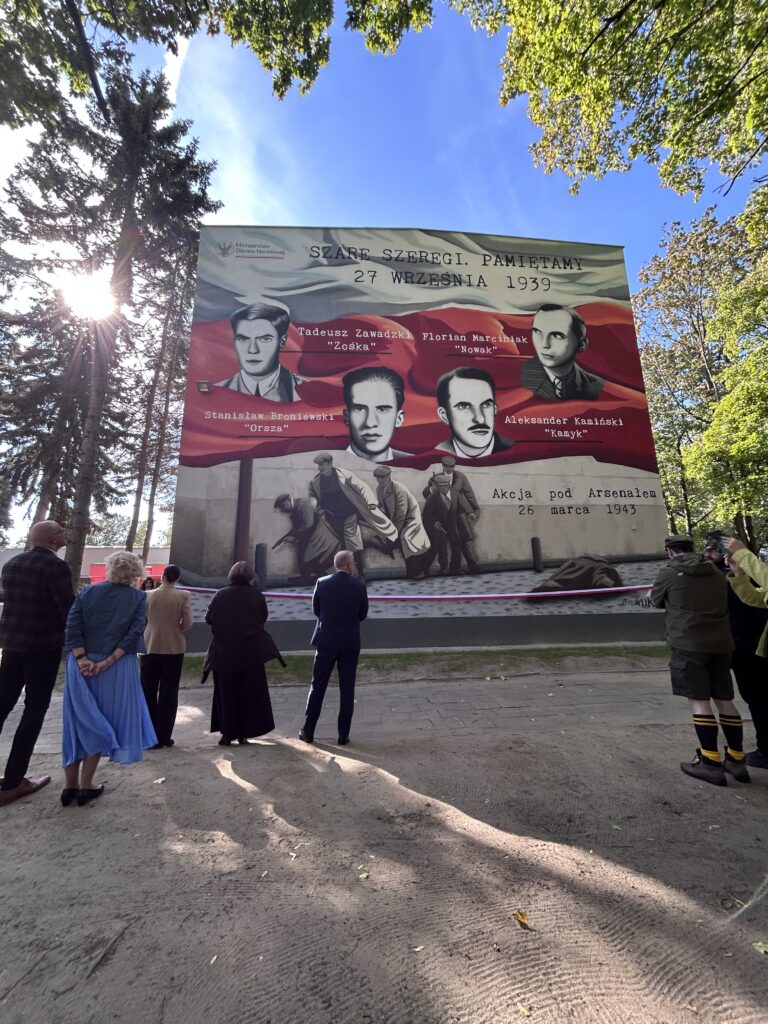 Na tym zdjęciu widzimy ludzi stojących pod muralem