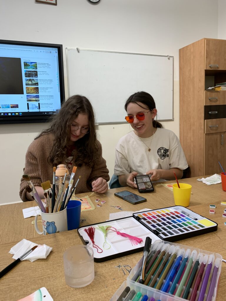 Fotorelacja z zajęć Zakładki do książek - malowane akwarelą, na zdjęciu widać dwie pracujące uczennice 