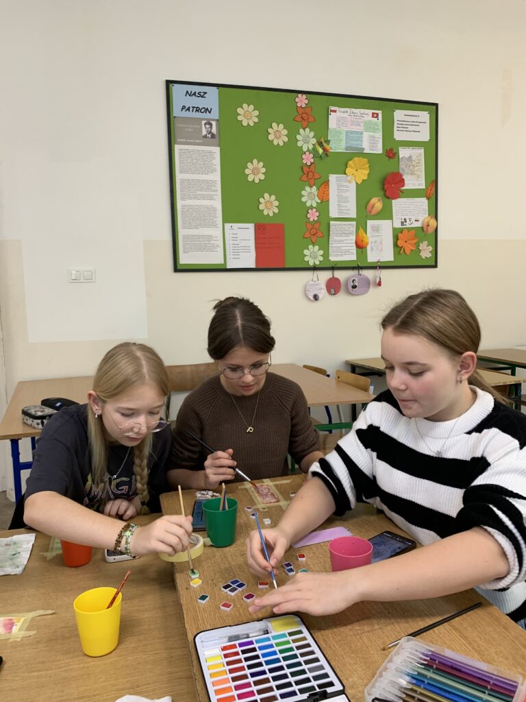 Fotorelacja z zajęć Zakładki do książek - malowane akwarelą, na zdjęciu widać trzy pracujące uczennice 