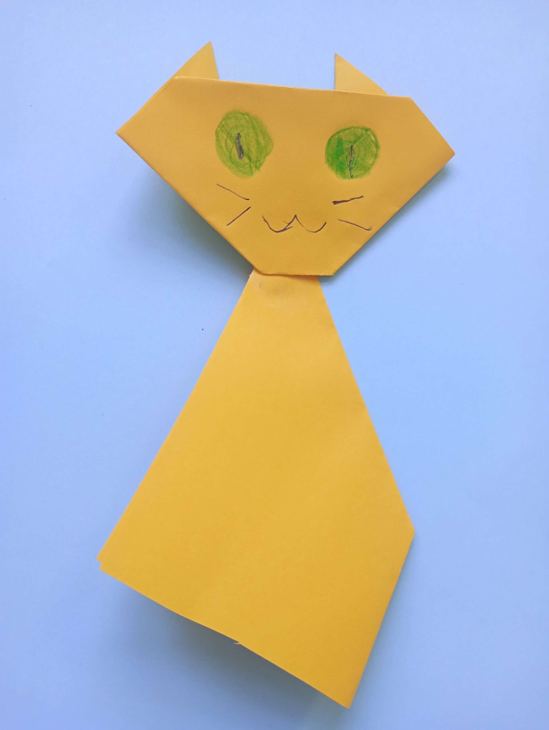 Obrazek przedstawia żółtego kota z papieru na niebieskim tle.