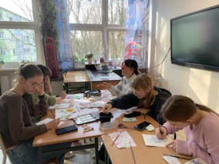 Dziewczyny z klasy 7 siedzące przy ławce malujące farbami