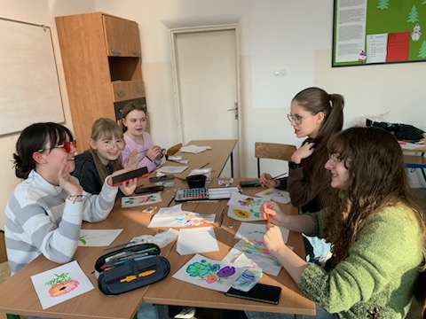Dziewczyny z klasy 7 siedzące przy ławce malujące farbami