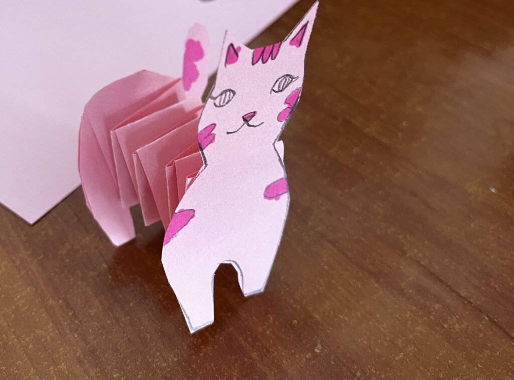 Obrazek przedstawia różowego kota z harmonijką jako tułów.