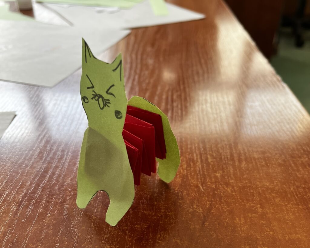 Obrazek przedstawia zielonego kota z harmonijką jako tułów.